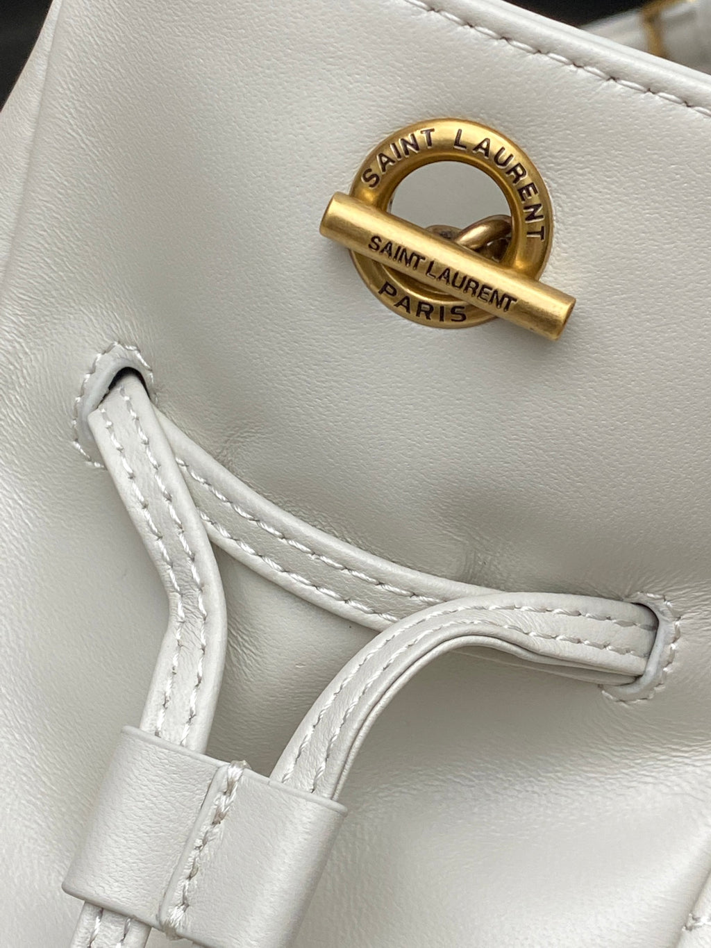 YSL bag close-up: gold Saint Laurent Paris emblem and white leather strap