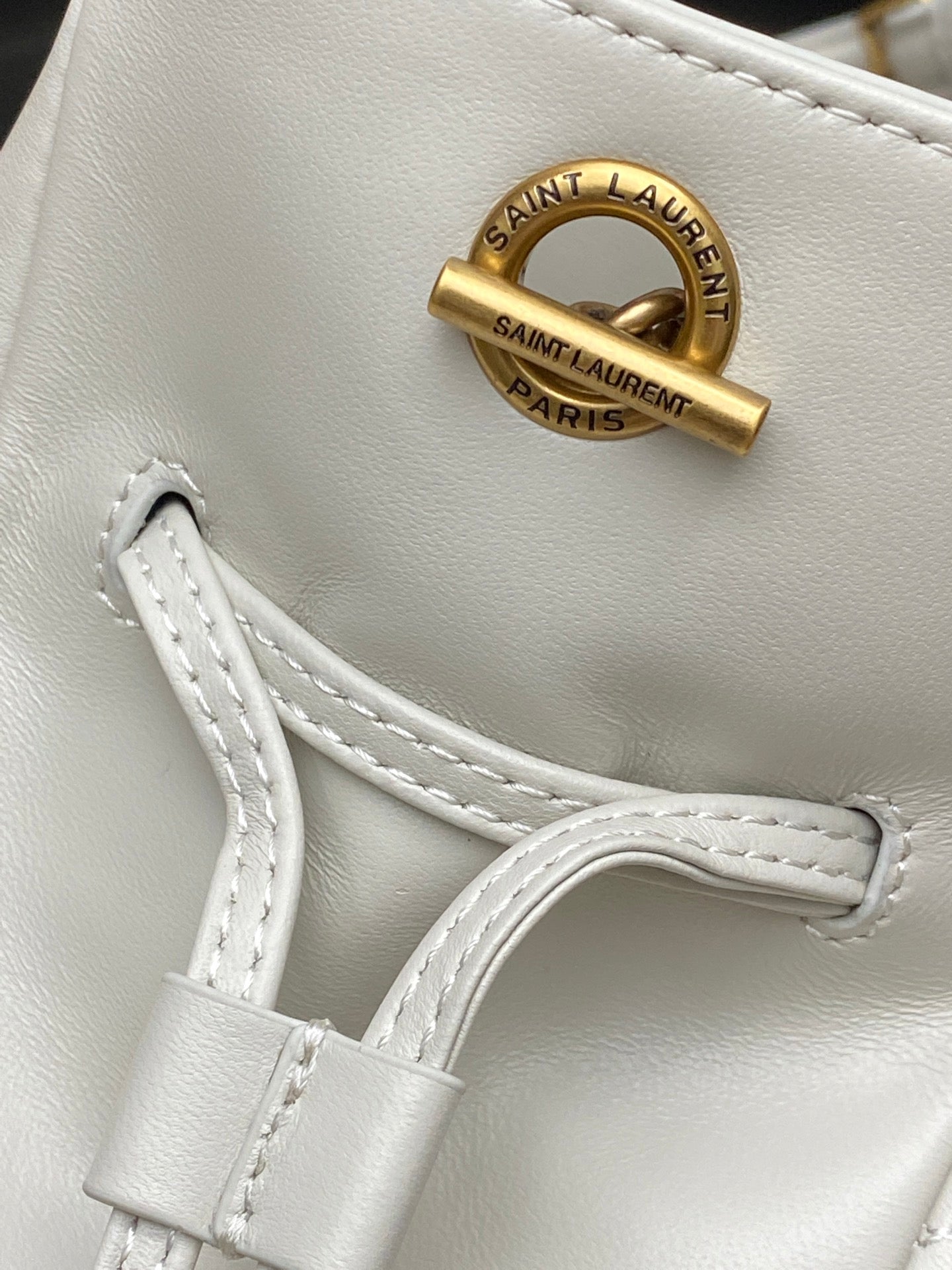 YSL bag close-up: gold Saint Laurent Paris emblem and white leather strap