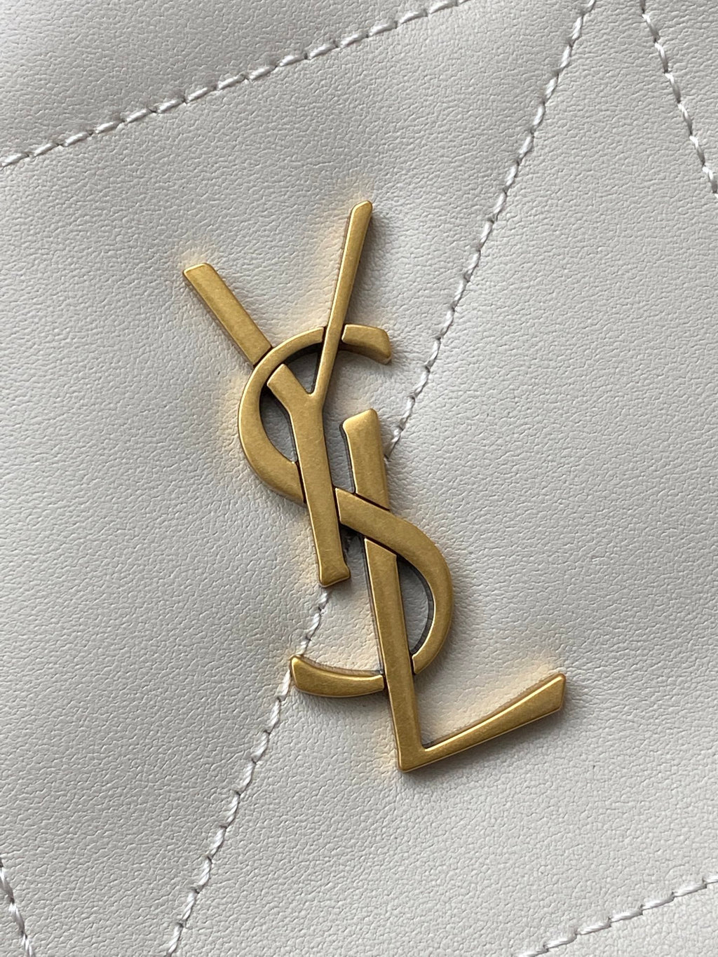 YSL bag close-up of gold YSL monogram on white quilted leather