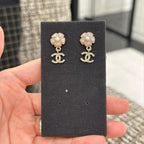 Gold-tone flower stud earrings with dangling logo, on black display card.