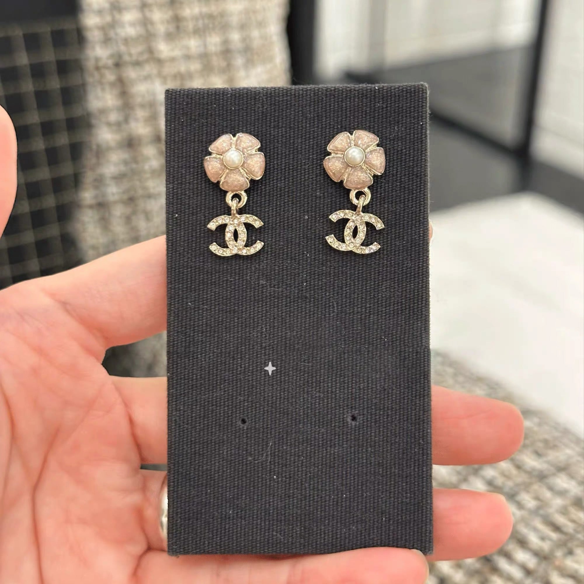 Gold-tone flower stud earrings with dangling logo, on black display card.