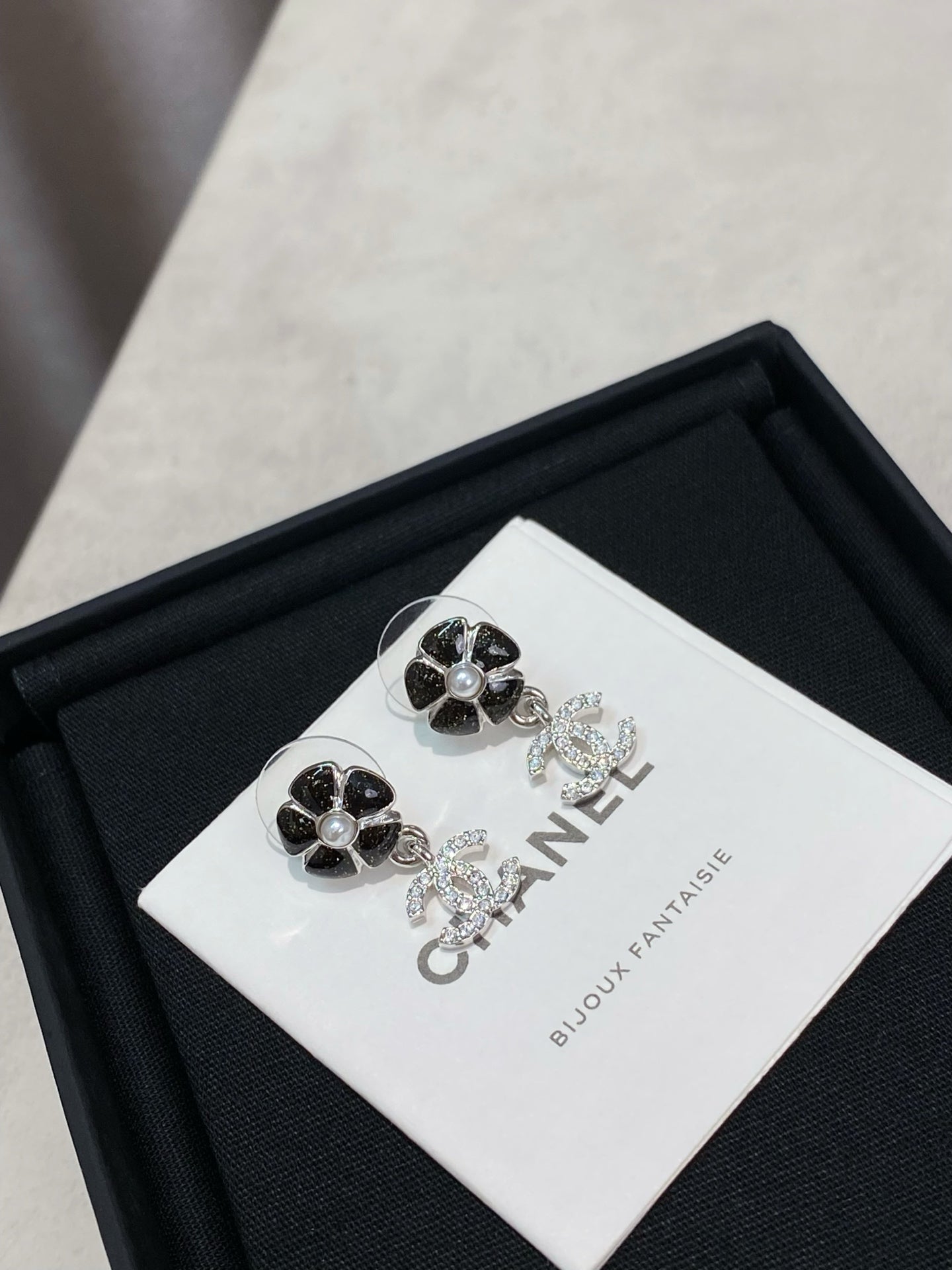Silver-tone flower stud earrings with dangling logo, on white CHANEL card in box.