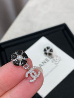 Silver-tone flower stud earring with dangling logo, held near a white CHANEL card.