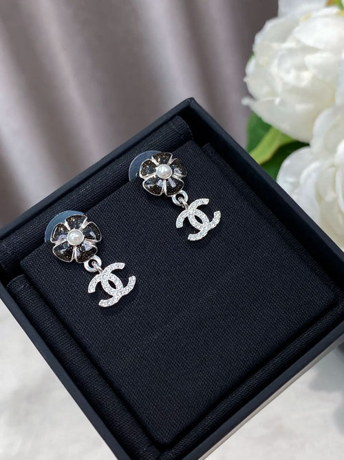 Silver-tone flower stud earrings with dangling logo, in a black jewelry box.
