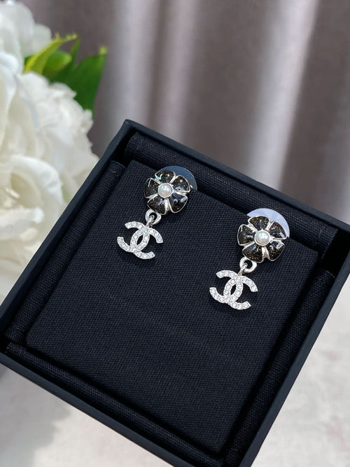 Silver-tone flower stud earrings with dangling logo, laid on black jewelry box.
