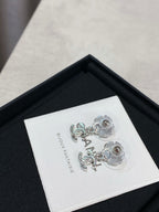 Silver-tone flower stud earrings with dangling logo, on white label inside black box.