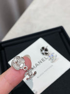 Silver-tone flower stud earrings with dangling logo, held near a CHANEL card.