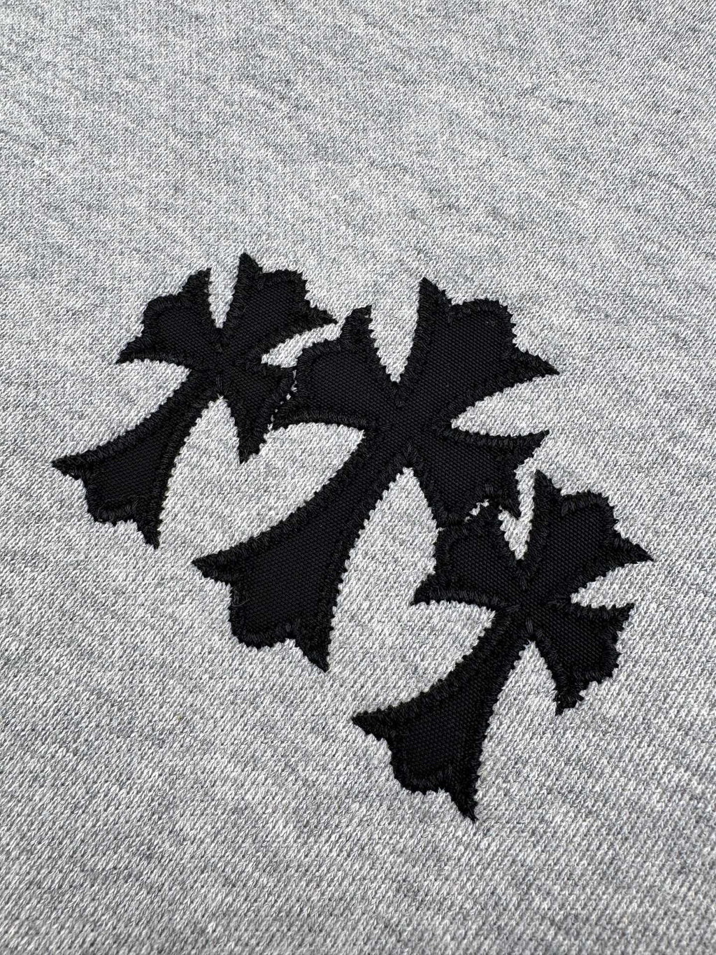 Gray hoodie fabric close-up with black embroidered logo.