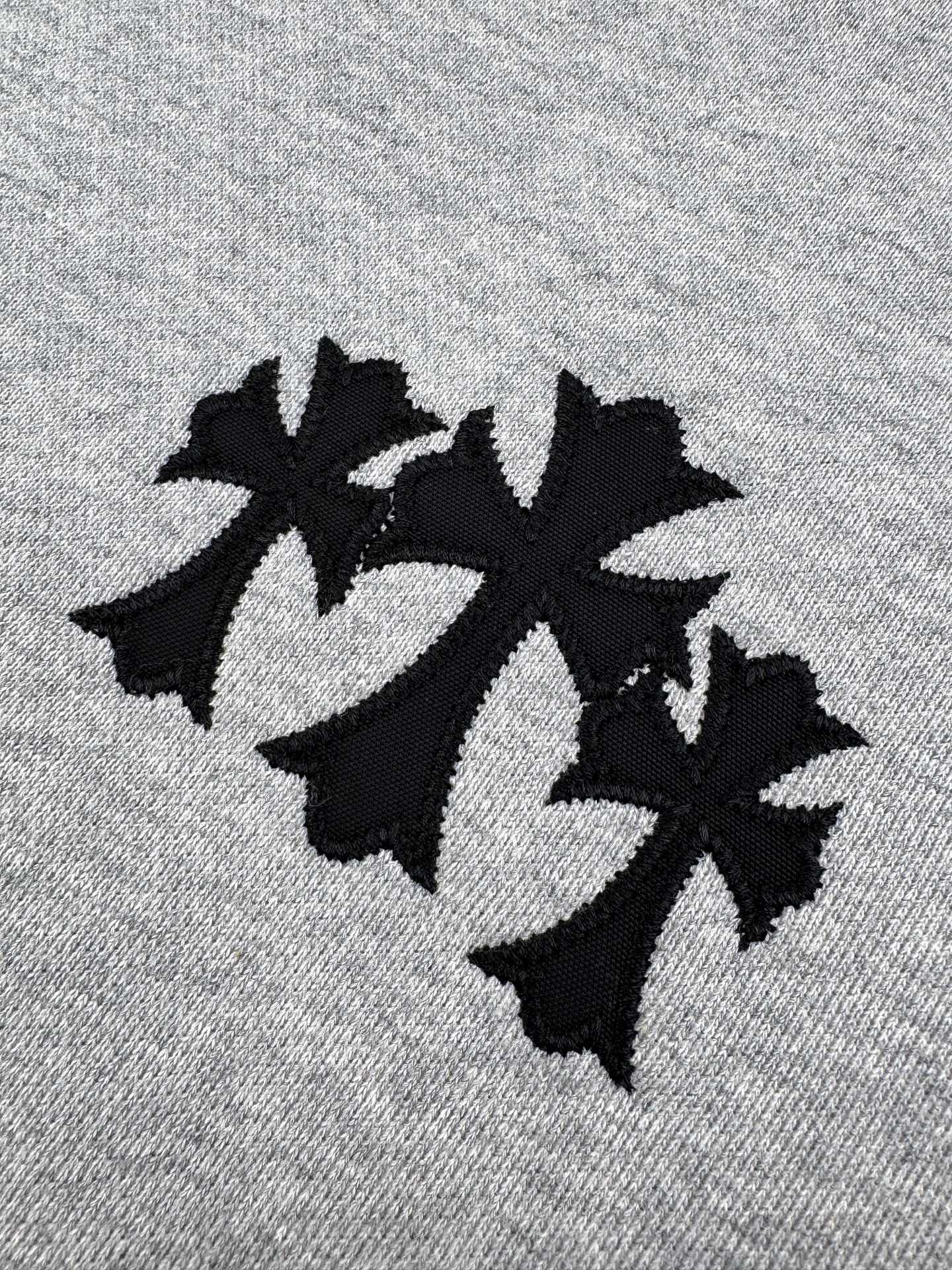 Gray hoodie fabric close-up with black embroidered logo.