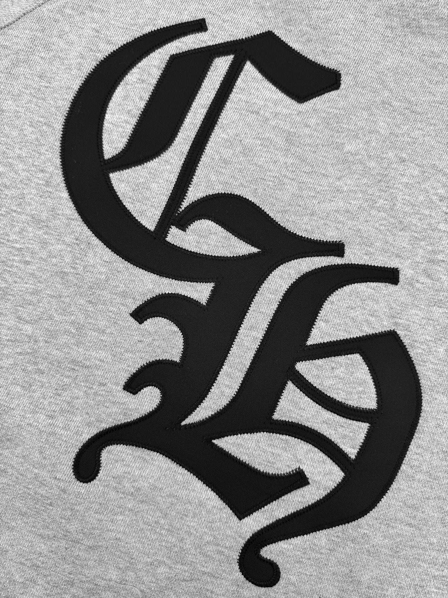Gray hoodie fabric close-up with large black logo graphic.