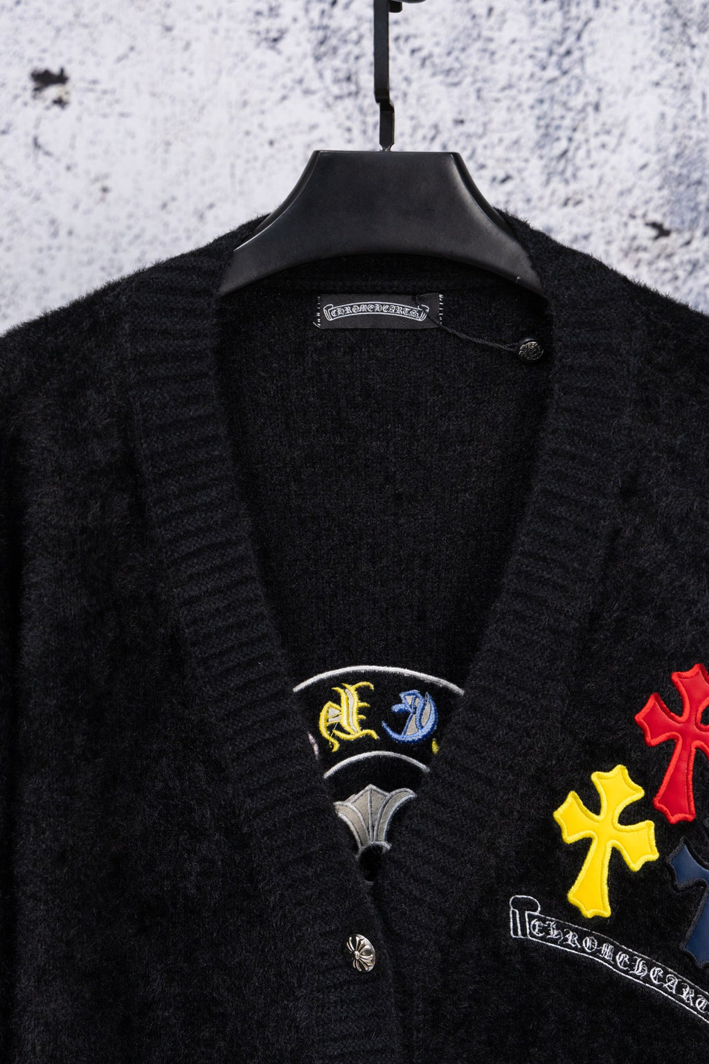 Black cardigan neckline with embroidered emblem patches and button front detail