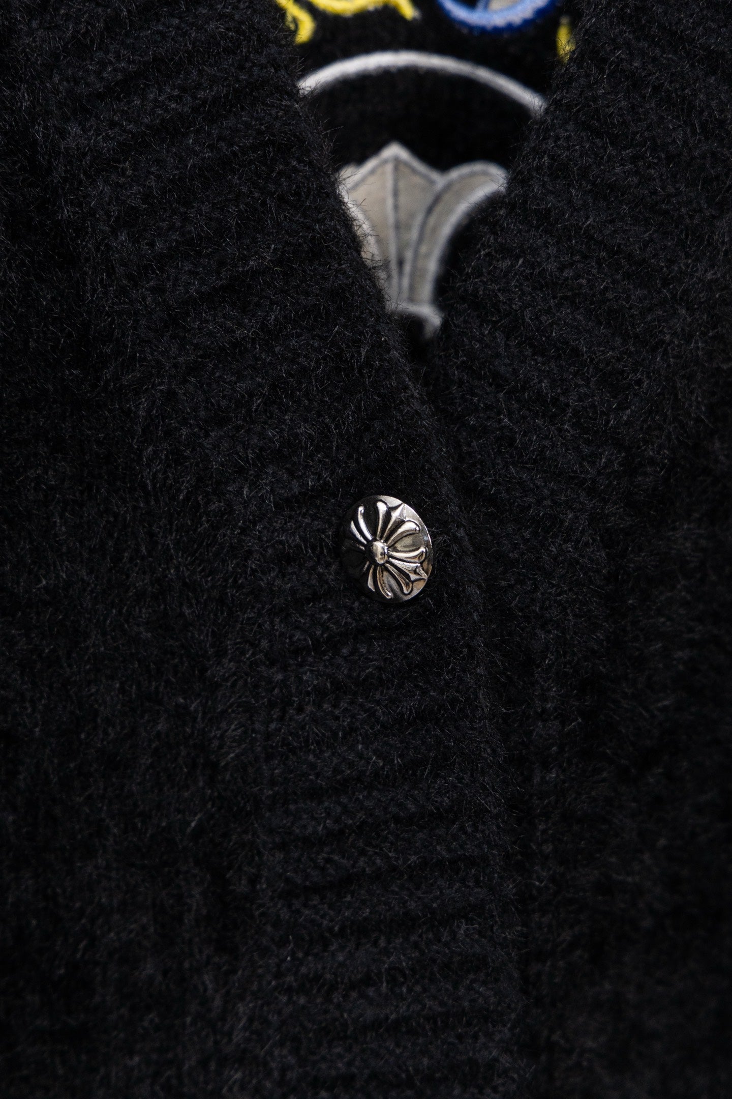 Black cardigan button placket with silver-toned button and embroidered insignia