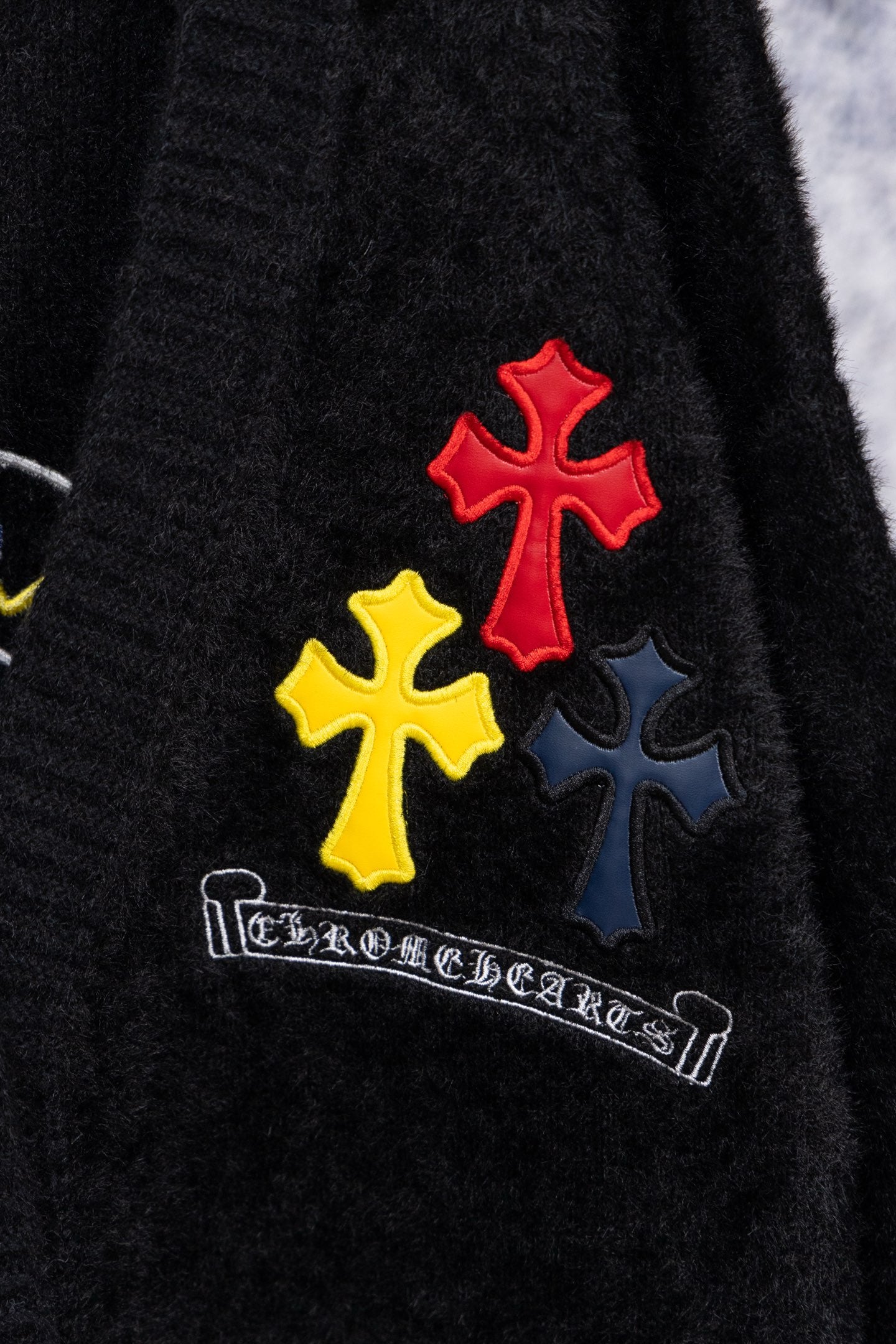 Black long-sleeve top with red, yellow, and blue cross patches and script logo