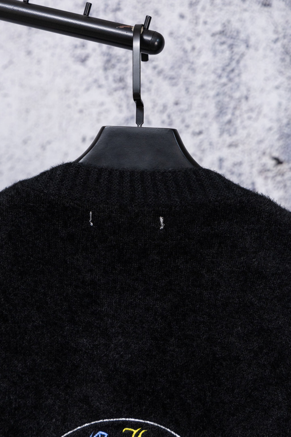Black cardigan back neckline with ribbed texture and small centered emblem