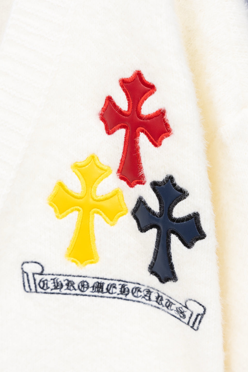 White cardigan sweater close-up of three cross appliques and embroidered banner