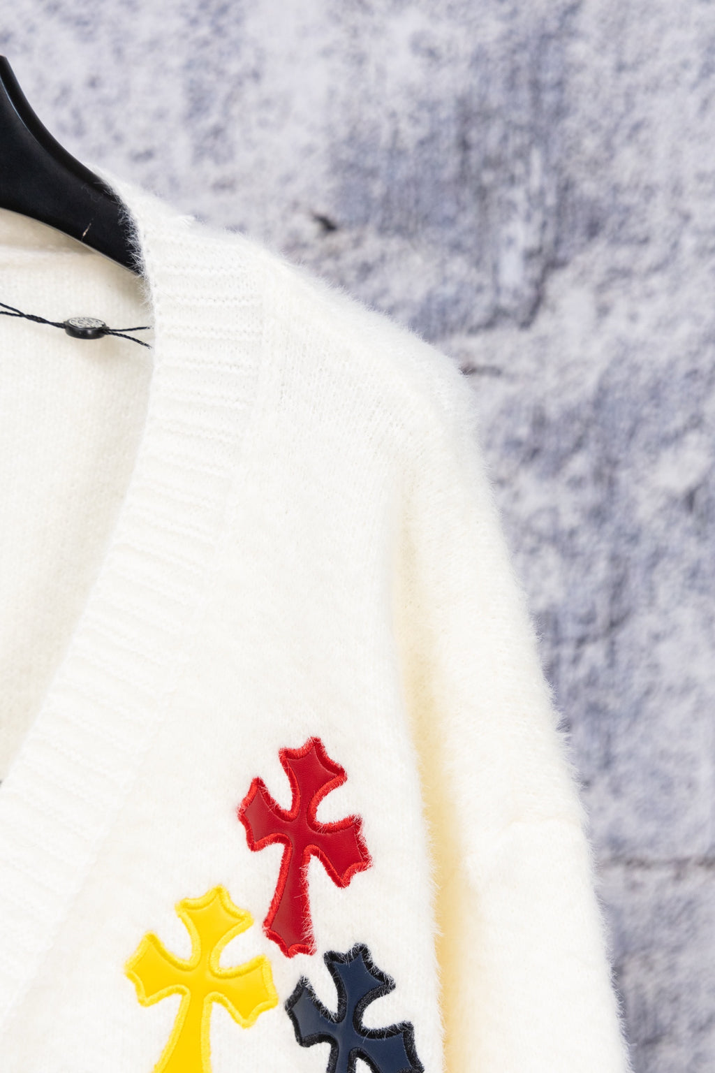 White cardigan sweater close-up of colorful cross appliques on sleeve