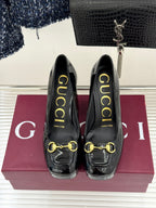 Black patent leather heeled pumps with gold chain horsebit detail, front view