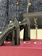 Glossy black patent leather high-heel pump with gold horsebit detail, angled