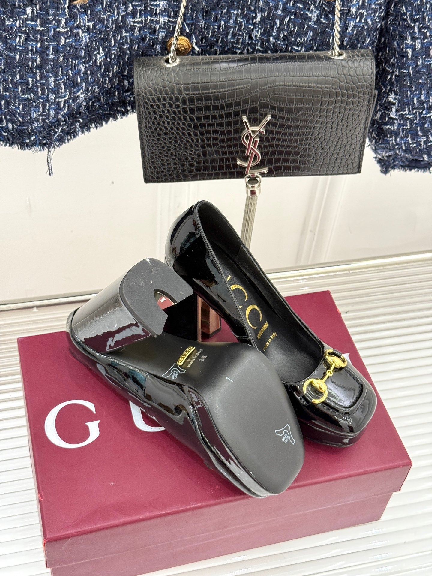 Black patent leather pumps with gold horsebit detail, pair on display