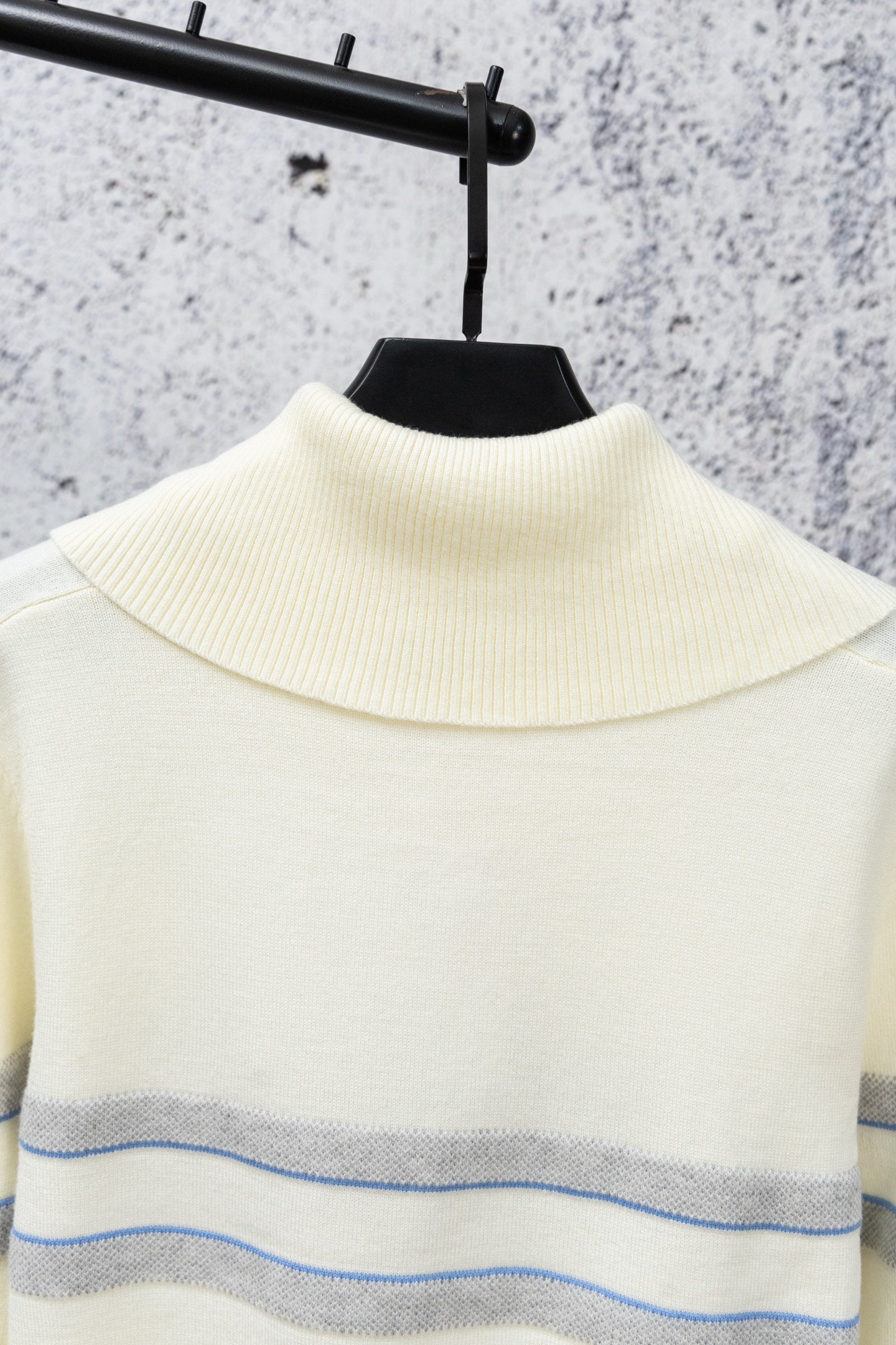 Cream sweater with high ribbed turtleneck and blue stripe band across chest