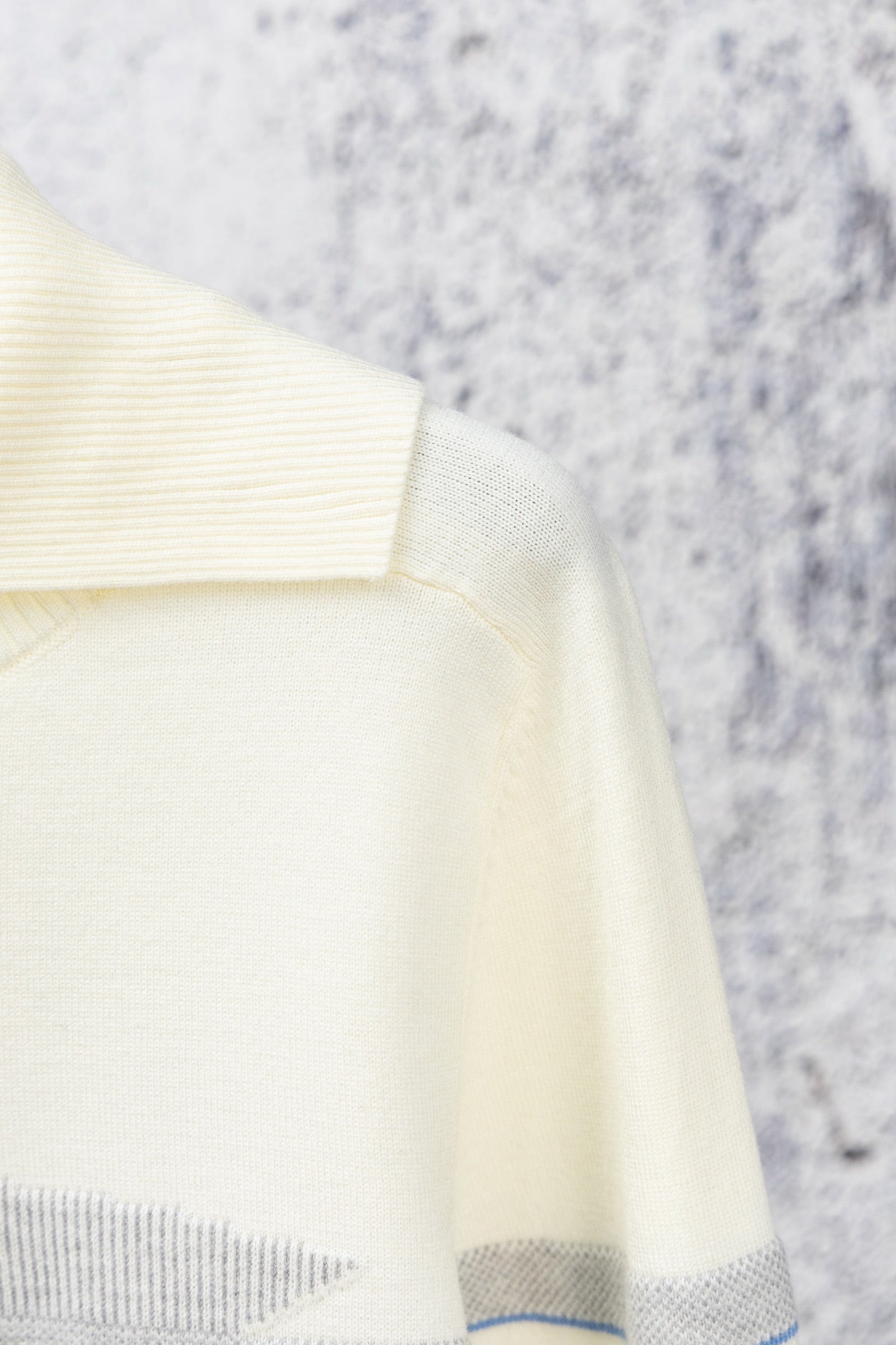 Cream sweater sleeve with ribbed cuff and blue stripe trim at hem