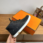 Hermes black lace-up sneaker held in hand on orange shoebox, white sole