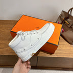 White lace-up sneakers held in hand, leather upper and gold H heel emblem