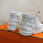 White mid-top sneakers from heel view, lace-up with gold H accent