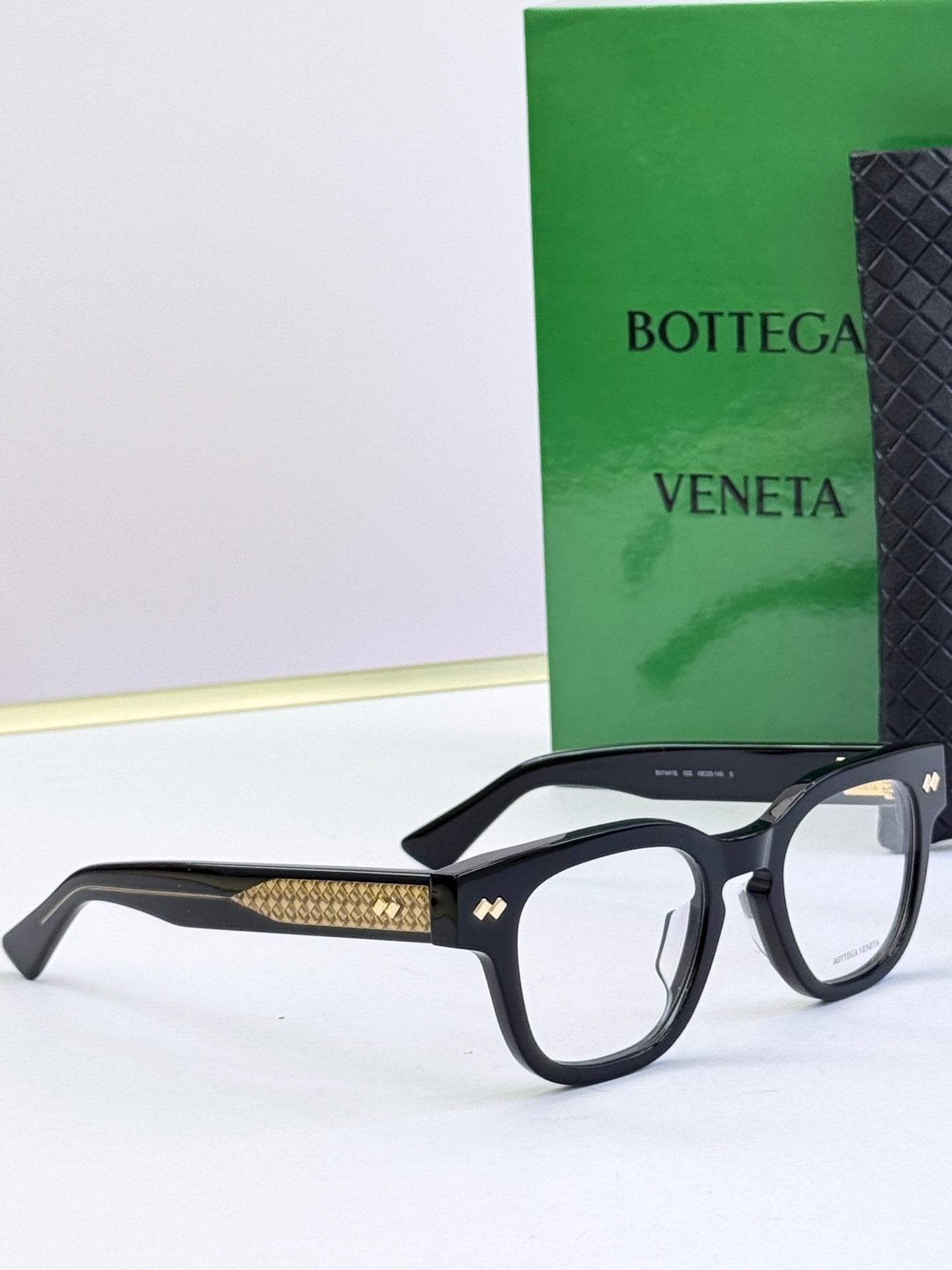 Bottega Veneta eyeglasses with black frames and gold textured side arms, profile view.