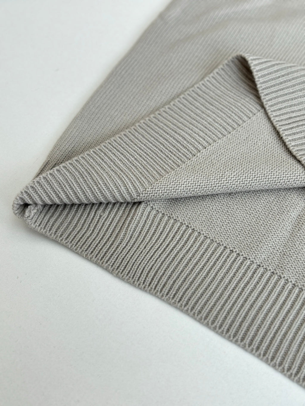 Light gray knit sweater detail: ribbed trim cuffs and folded hem