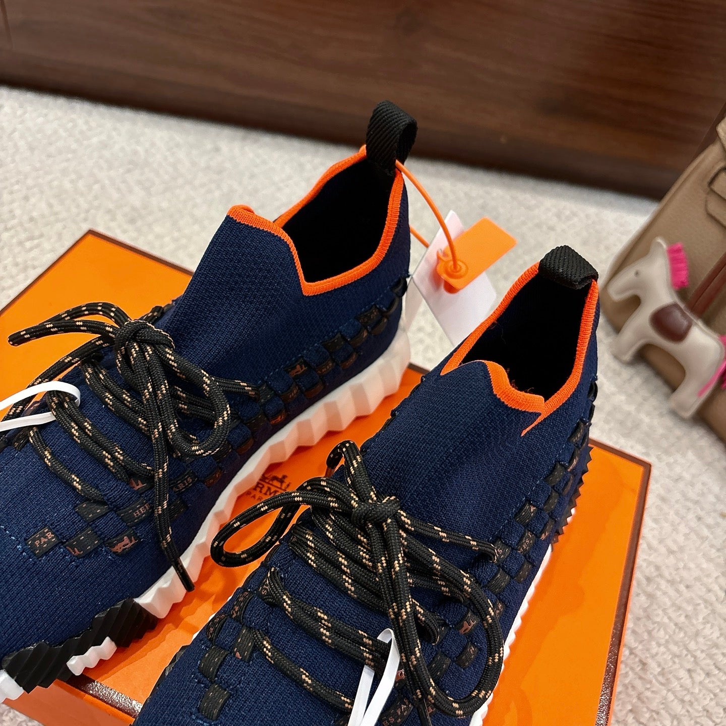Hermes unisex sneakers in navy with orange collar trim, black laces, white cushioned sole.