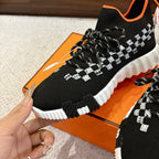 Hermes unisex sneaker close-up: black knit, white checker pattern, orange collar trim, laces