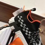 Hermes unisex sneaker close-up: black knit, white checker strap, orange collar piping, textured sole