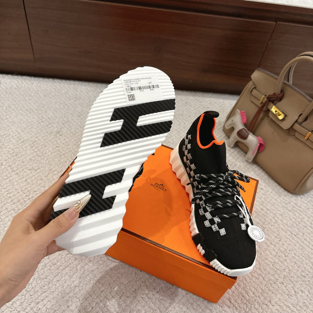 Hermes unisex sneaker outsole view: black upper with orange trim, white ridged tread sole