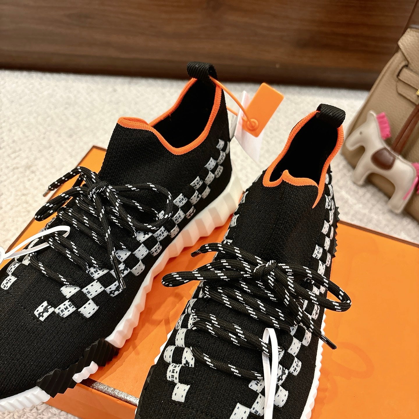 Hermes unisex sneakers close-up: black knit with white check panel, orange trim, braided laces