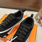 Hermes unisex black sneakers front view, black laces and white side stripe, round emblem