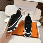 Hermes unisex black sneakers angled view, white edging, lace-up, thick tread sole