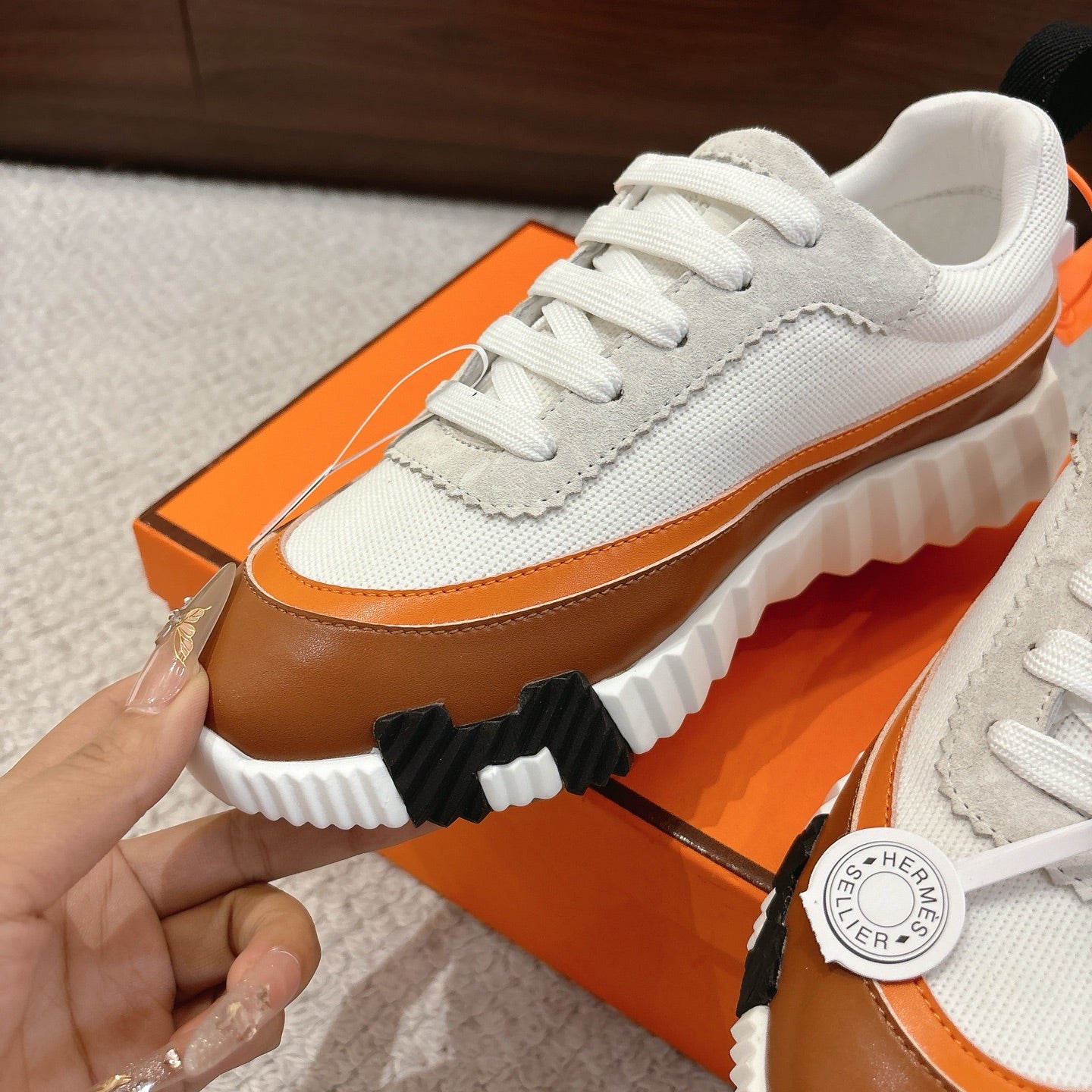 Close-up of Hermes unisex sneakers: white mesh upper, brown side stripe, chunky sole