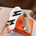 Hermes unisex sneaker outsole view: black traction pattern with white ridged sole and beige upper.
