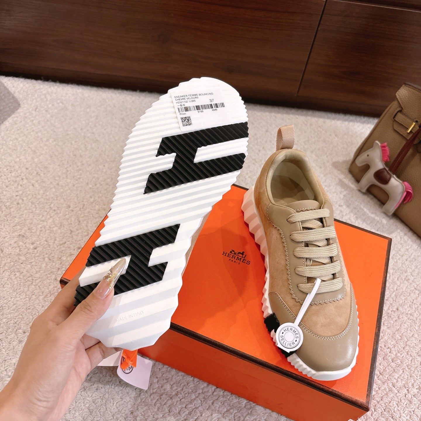 Hermes unisex sneaker outsole view: black traction pattern with white ridged sole and beige upper.