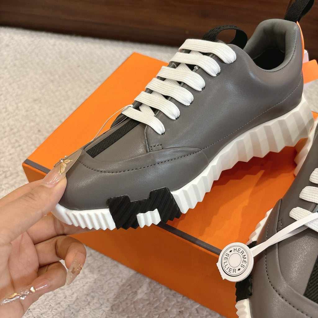 Hermes gray sneaker close-up with white laces, black detail patch, and chunky sole