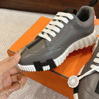 Hermes gray sneaker close-up with white laces, black detail patch, and chunky sole