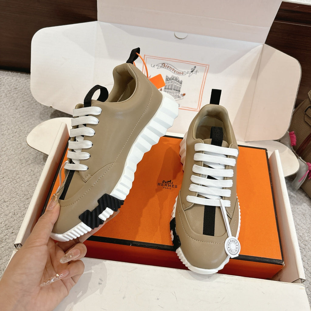 Beige unisex sneakers pair in box, with white laces, black panels, and ridged white soles.