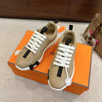 Beige unisex sneakers with white laces and black accents, shown on orange shoe box.