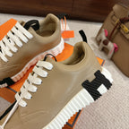 Beige unisex sneakers with white laces, black side details, and orange-box packaging.