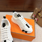 White Hermes low-top sneakers with black center panel and lace-up, angled side view.