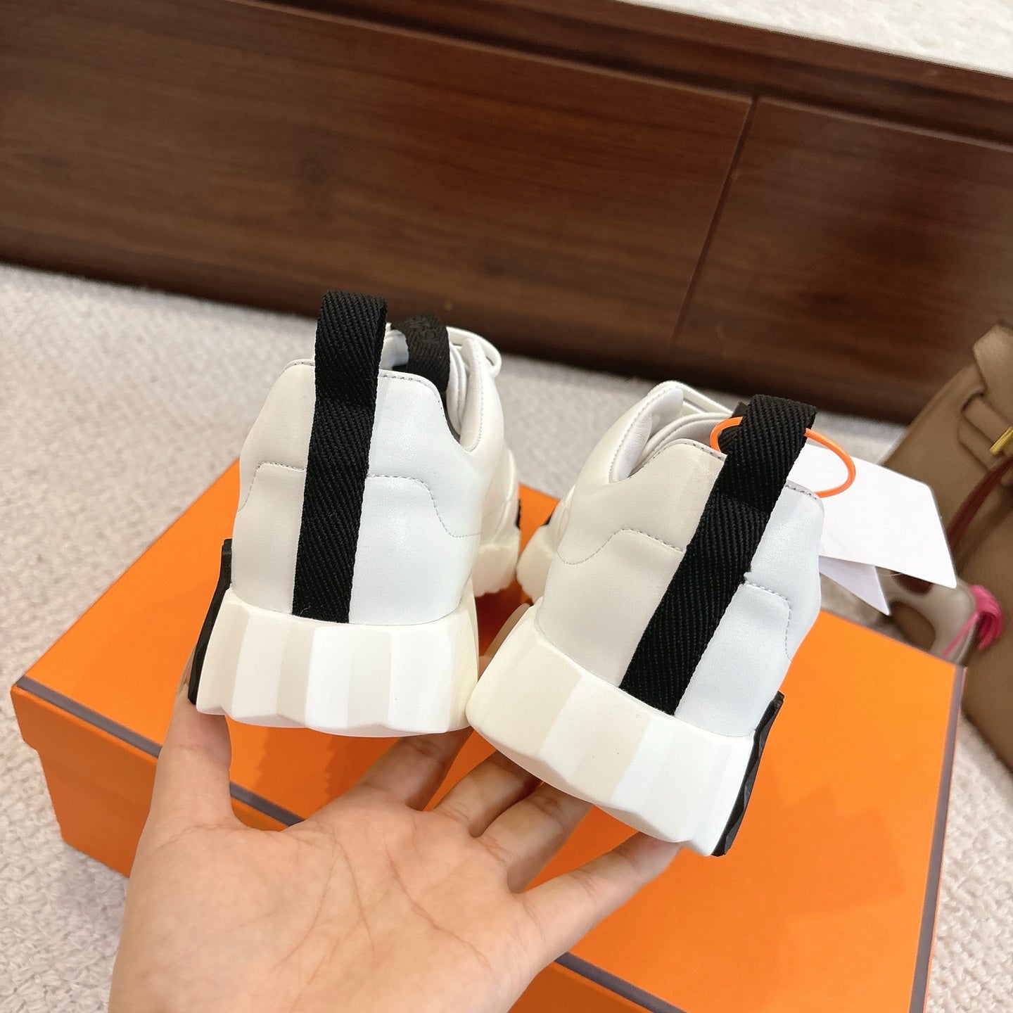 White Hermes sneakers with black heel strap detail and cushioned sole, back view.