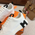 White Hermes sneakers with black stripe accents and lace-up, close-up side angle.