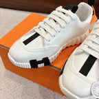 White Hermes sneakers with black side panel and lace-up, close-up on chunky sole.
