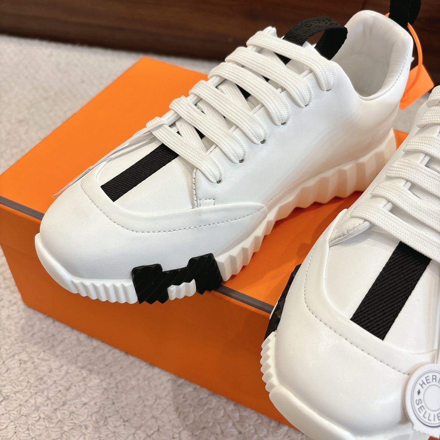 White Hermes sneakers with black side panel and lace-up, close-up on chunky sole.